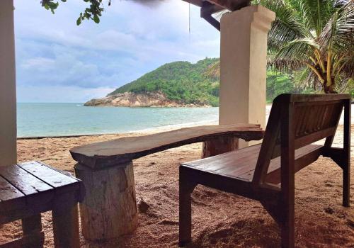 a wooden bench sitting on a beach near the ocean at Mai Pen Rai Bungalows in Than Sadet Beach