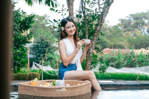 una donna seduta su un cesto che tiene in mano una tazza di caffè di Premadhan Cottage Canggu a Canggu