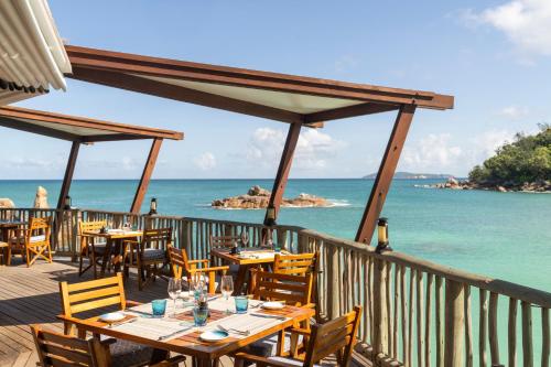 a restaurant with tables and chairs on a deck overlooking the ocean at Constance Lemuria in Grand'Anse Praslin