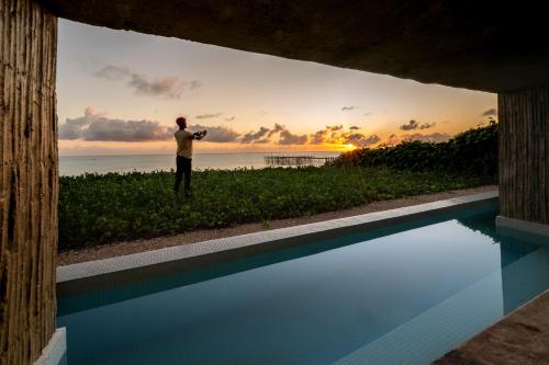 a man standing next to a swimming pool with the sunset at Bamboo Zanzibar in Jambiani