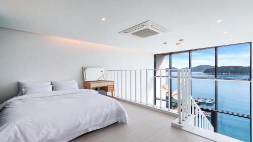 a white bedroom with a bed and a large window at Tongyeong FH365 Pension in Tongyeong