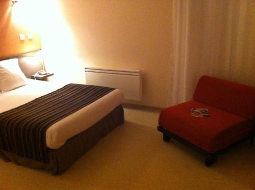 a hotel room with a bed and a red chair at Fasthôtel Le Râle Des Genêts - Un hôtel FH Collection in Dun-sur-Meuse