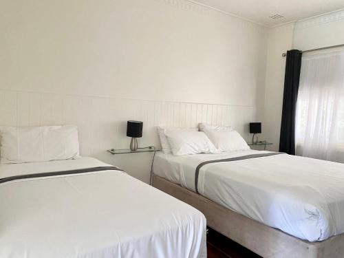 two beds in a bedroom with white walls and a window at Paradise Motel Busselton in Busselton