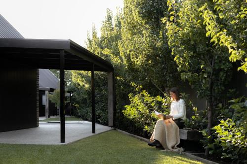 a woman sitting on a bench reading a book at Vale 194 - Luxury Accommodation in McLaren Vale - 5 holiday homes with king size beds in McLaren Vale