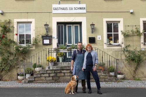 a man and woman standing in front of a building with a dog at Gasthaus zum Schwan in Castell