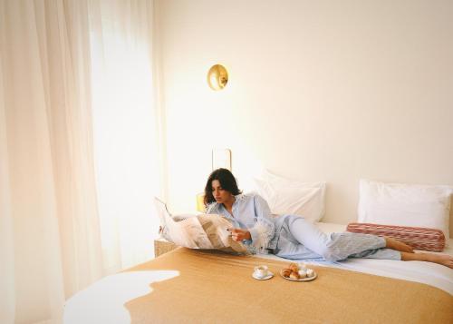 a woman sitting on a bed reading a book at Apollo Palm Hotel in Athens