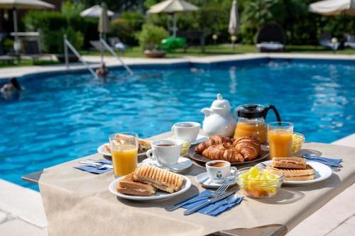 a table with breakfast foods and drinks next to a pool at DB Villas Le Ville del Lido Resort in Venice-Lido