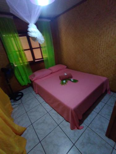a room with a pink bed and green curtains at Maupiti Authentique in Te-Fare-Arii