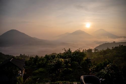 a view of a misty valley with mountains and the sun at Pondok Devana Kintamani in Kintamani