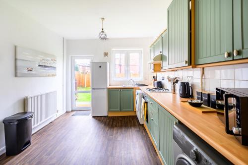 a kitchen with green cabinets and a white refrigerator at Trafford Eden - 3 Bed Home near Old Trafford and Trafford Centre with Free Parking in Manchester