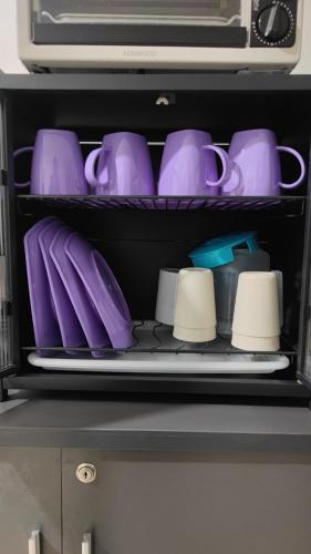 a shelf with purple cups and mugs on it at Homestay Atok Mus'lim Only in Jenjarum