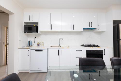 a white kitchen with white cabinets and a glass table at Glenelg North House, 3QBed, 2KSBed, 2Bth, 5TV in Glenelg