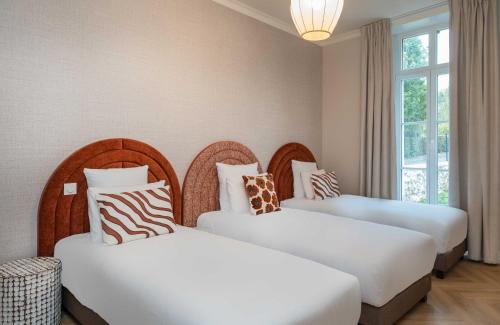 two beds in a hotel room with white sheets and zebra pillows at L'Horloge - Appart'Hotel proche de Disneyland in Montévrain