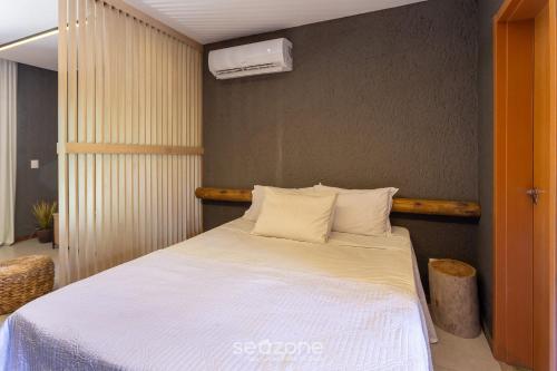 a bedroom with a bed with white sheets and a fan at Studio em Cond. c/ piscina próx. da praia CVKB0006 in São Miguel dos Milagres