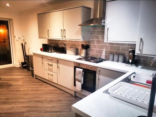 a kitchen with white cabinets and a stove top oven at 2 Bed Bungalow - Parking - New Build - High End Furnishings - Wheel Chair Accessible - Large Enclosed Garden - Dog Friendly in Rotherham