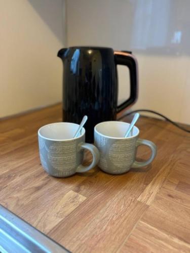 two cups sitting on a table with a coffee pot at Modern apartment in Stenhousemuir in Stenhousemuir