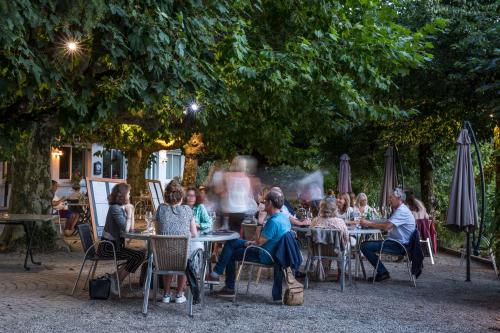 a group of people sitting at tables under a tree at Hotel Les Mésanges in Saint-Martin-dʼUriage