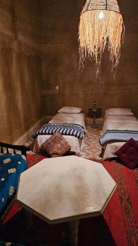 a room with two beds and a table and a chandelier at Nomad Merzouga Desert House in Hassilabied