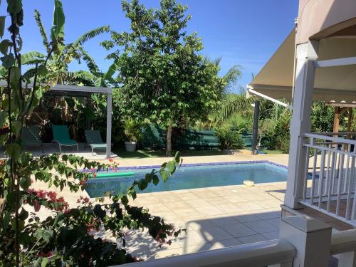 a swimming pool with chairs and a tree next to a house at VILLA ALIZEE APPARTEMENT N°6 in Sainte-Rose