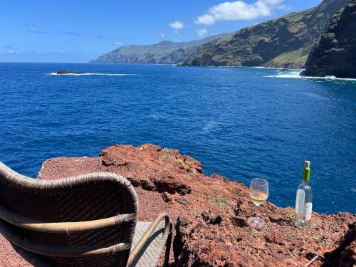 a bottle of wine and a chair sitting on a rock near the ocean at Casa Rural Cueva Las Varas in El Mudo