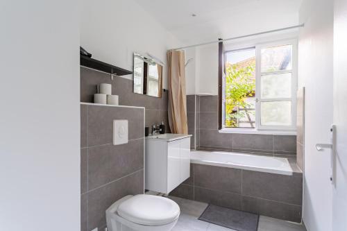 La salle de bains est pourvue de toilettes, d'une baignoire et d'une fenêtre. dans l'établissement Confort au cœur de Strasbourg, à Strasbourg