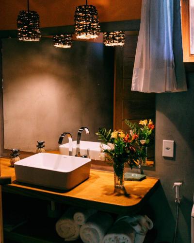 a bathroom with a sink and flowers on a counter at Hospedaria Dedo de Moça in Praia do Espelho