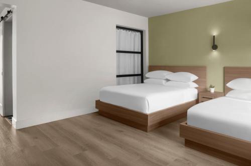 two beds in a room with white walls and wooden floors at The Lum Hotel Los Angeles Stadium District in Inglewood