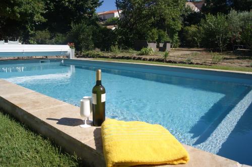 a bottle of wine and a glass next to a swimming pool at Le Petit Molière in Servian