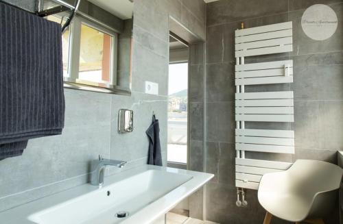 a bathroom with a white sink and a chair at Sky Panorama Apartman Pécs in Pécs