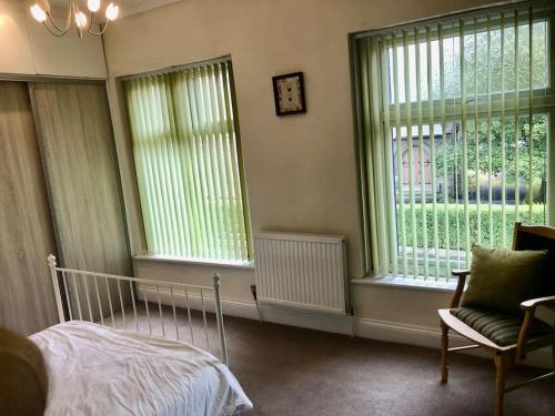 1 Schlafzimmer mit einem Bett, 2 Fenstern und einem Stuhl in der Unterkunft Cheerful 2 bedroom town house in Lancashire in Chorley