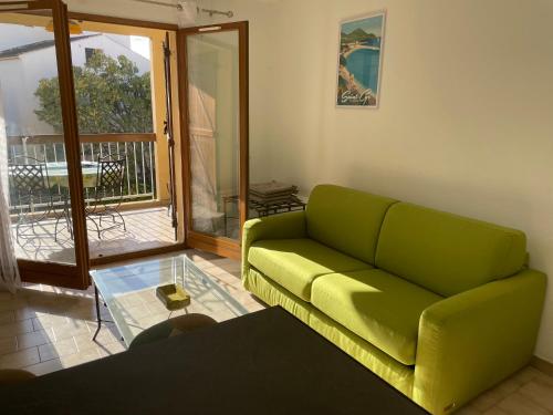 Il comprend un salon avec un canapé vert et un balcon. dans l'établissement Appartement T2 avec piscine, à Sanary-sur-Mer