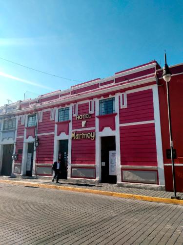 a red and white building with a man walking past it at Hotel Marmoy in Cholula
