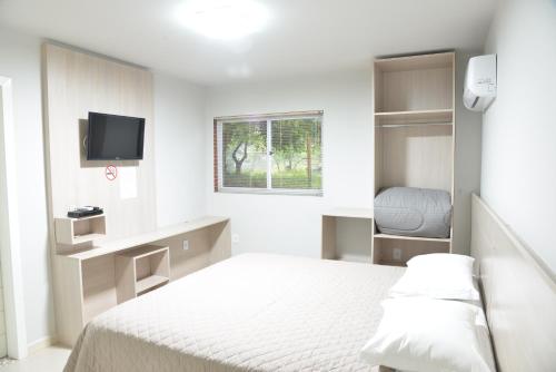 Dieses weiße Zimmer verfügt über ein Bett und einen TV. in der Unterkunft Hotel Guerra - Pousada Montebelo in Jaguaruna