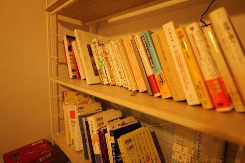 a row of books sitting on a shelf at yol Guesthouse ヨルゲストハウス in Takeo