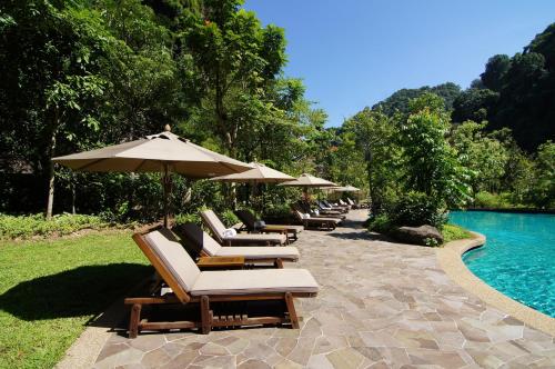 a group of lounge chairs and umbrellas next to a pool at The Banjaran Hotsprings Retreat in Ipoh