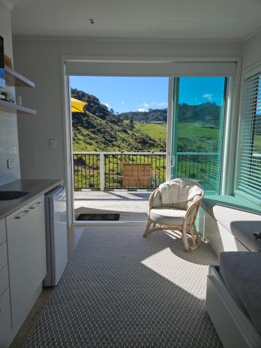 a kitchen with a chair and a view of a balcony at Waihi beach Toroha cosy cabin in Waihi Beach