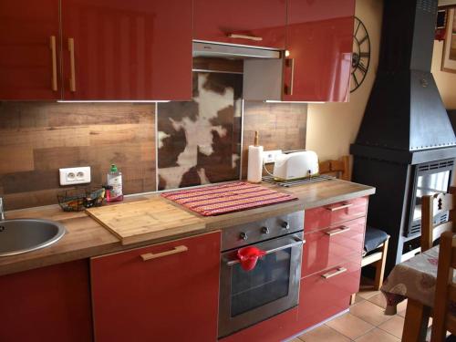 La cuisine est équipée de placards rouges et d'un four avec plaques de cuisson. dans l'établissement Chalet chaleureux avec poêle à bois et parking, proche du centre de Font-Romeu - FR-1-580-124, à Font-Romeu-Odeillo-Via