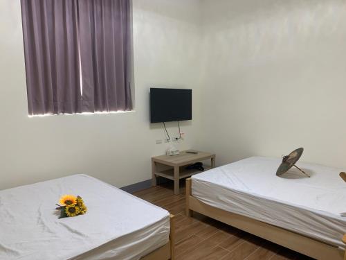 two beds in a room with a tv and flowers at Hakka Eco-farm 雅歌園民宿食農教育有機農場 in Wanluan