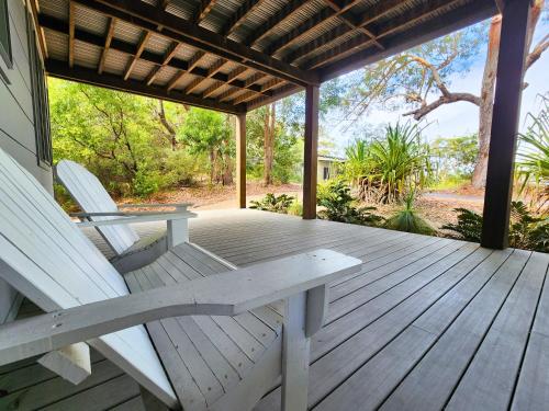 a porch with two white chairs and a table at Sandy Escape Holiday House Kingfisher Bay Resort in Kingfisher Bay