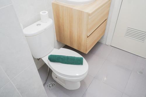 a bathroom with a toilet with a green towel on it at Cozy and Spacious 1BR Apartment at Parkland Avenue By Travelio in Tangerang