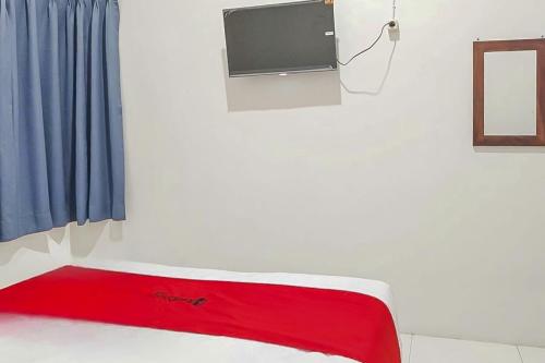 a bed with a red blanket and a tv on a wall at RedDoorz at Anjasmoro Guest House near Bandara Ahmad Yani Semarang in Kalibanteng-lor