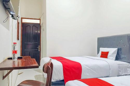 a bedroom with two beds and a table and a door at RedDoorz at Anjasmoro Guest House near Bandara Ahmad Yani Semarang in Kalibanteng-lor