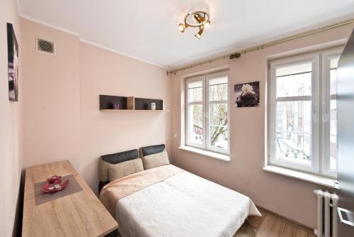 a bedroom with a bed and a table and windows at Gdańskie Apartamenty - Apartament Szeroka in Gdańsk