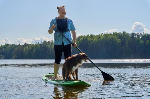 a woman standing on a paddle board with a dog at Lakeside Villa next to Nuuksio National Park, in addition Hot Tub and Breakfast in Otalampi
