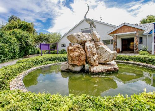 a statue of rocks in a pond in front of a house at SleepOver Lanseria in Lanseria