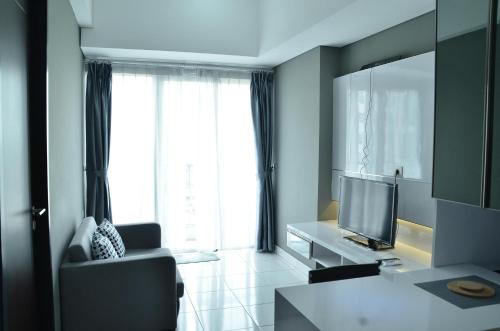 a living room with a couch and a television at Homey and Comfy 1BR at Casa de Parco Apartment By Travelio in Tangerang