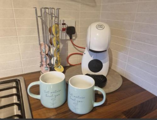 two coffee mugs on a counter next to a coffee maker at The Bracken's by Ritual Stays in Hemel Hempstead
