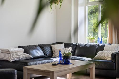 a living room with a black leather couch and a wooden coffee table at Boerderij de Borgh in Westerbork