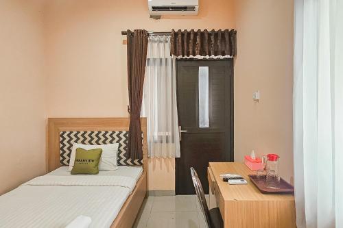 a small room with a bed and a table and a door at Urbanview MJ House Syariah Bandung in Bandung