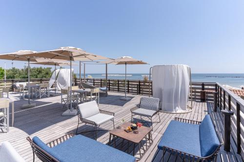 a deck with chairs and tables and umbrellas on the beach at Club del Sole Vigna sul Mar Family Collection in Lido di Pomposa